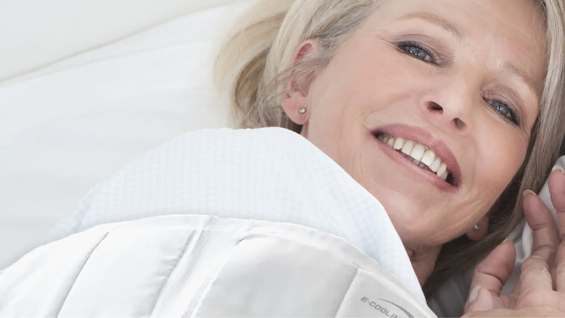 Blonde Frau mittleren Alters im Bett liegend mit der E.COOLINE aktiv kühlenden Bettdecke