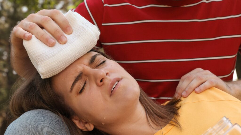 Hitzebelastungen in Unternehmen muessen gemeistert werden: Junge Frau mit Hitzeproblemen bekommt ein kühles Tuch auf die Stirn